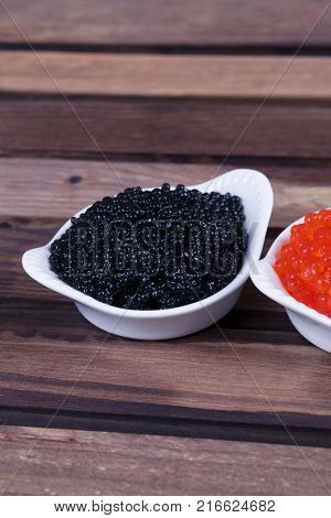 black sturgeon hausen caviar with red salmon caviar in white bowls on wooden background