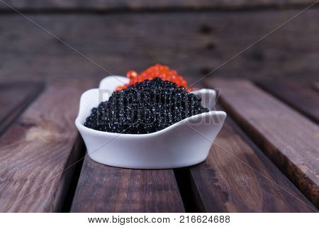 black sturgeon hausen caviar with red salmon caviar in white bowls on wooden background