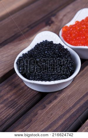 black sturgeon hausen caviar with red salmon caviar in white bowls on wooden background