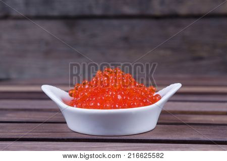 red salmon caviar in white bowls on wooden background