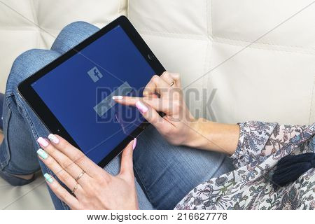 Sankt-Petersburg Russia December 3 2017: Woman Hands using iPad pro with Facebook homepage on monitor screen. Facebook the biggest social network website. Homepage of Facebook.com on tablet computer.