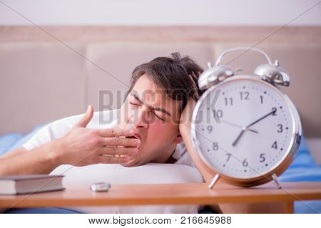 Man in bed frustrated suffering from insomnia with an alarm cloc