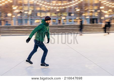Outdoor Shot Of Unexperienced Male Skater Uses Skate Aid For Go Skating On Ice, Being In Good Mood,