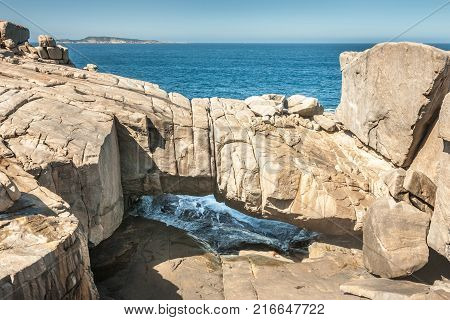 Albany WA Australia - November 23 2009: Beige huge Gapanda Bridge Rock In Torndirrup National Park with blue ocean under and above on coastline of Great Australian Bight. Small stroke of blue sky.