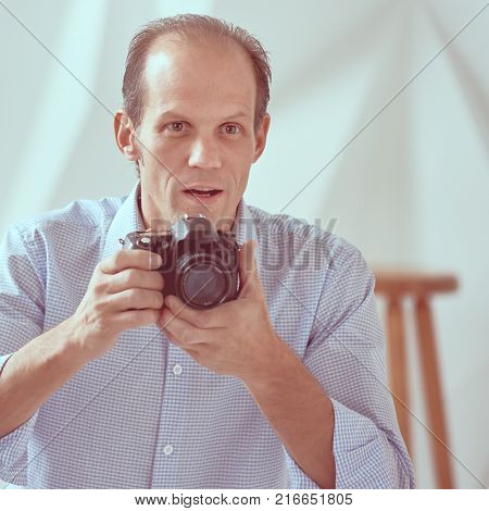 Young professional photographer taking photos in modern studio, image with vintage toning