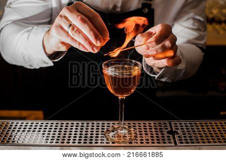 Bartender in white shirt making a fresh burning cocktail with a smoky note on the bar counter