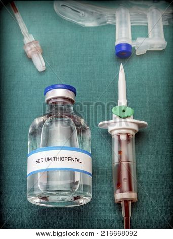 Rubber drip irrigation system with traces of blood along with vial of sodium thiopental, conceptual image