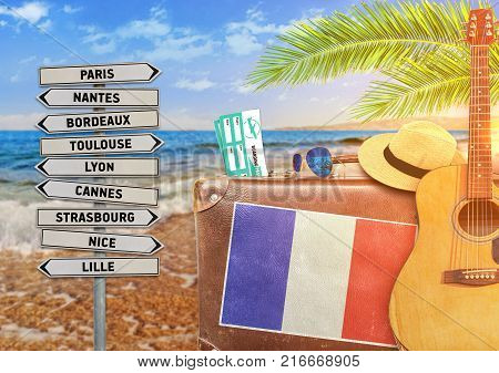 Concept of summer traveling with old suitcase and France town sign with burning sun