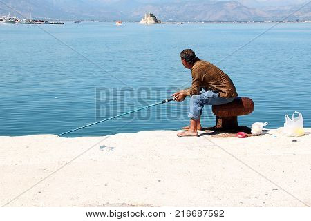 NAFPLIO, GREECE - SEPTEMBER 20, 2012: An unidentified man is fishing on a port pier in the hot noon.