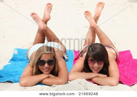 Dia na praia: duas meninas, encontrando-se em seus estômagos com pernas cruzaram