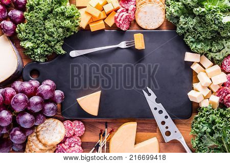 Meat and Cheese plate with a black cutting board. Various cheeses and meats are displayed with kale and purple grapes.