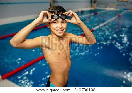 Portrait of fit young boy wearing swimming goggles at the pool. Portrait of a smiling boy swimmer wearing swim goggles at swimming pool. Happy fit child at pool looking at camera.