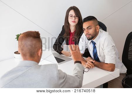 Concentrated employees using devices at meeting to share recourse or information. Serious young colleagues listening to coworkers idea. Technology concept