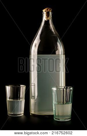 Ukrainian national drink. The big bottle of moonshine isolated on black background. Old bottle and glass with russian vodka.