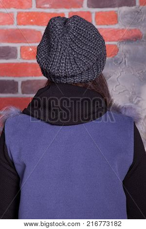 girl in hat and fur coat, against a brick wall background