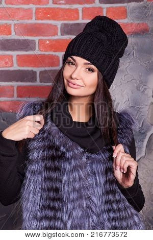 girl in hat and fur coat, against a brick wall background