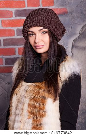 girl in hat and fur coat, against a brick wall background