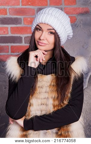 girl in hat and fur coat, against a brick wall background