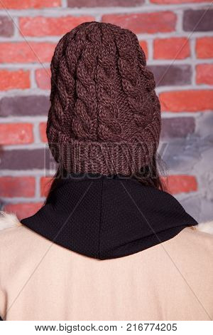 girl in hat and fur coat, against a brick wall background