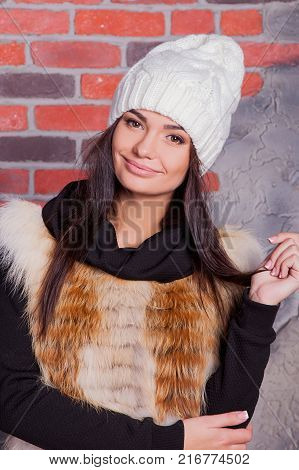 girl in hat and fur coat, against a brick wall background