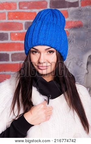 girl in hat and fur coat, against a brick wall background