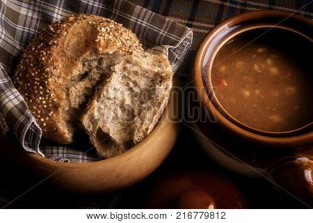 Food, a soup broth  and seeded Roll winter warming lunch, showing a rustic food scene with wooden bread dish and earthenware crockery soup dish with lid.