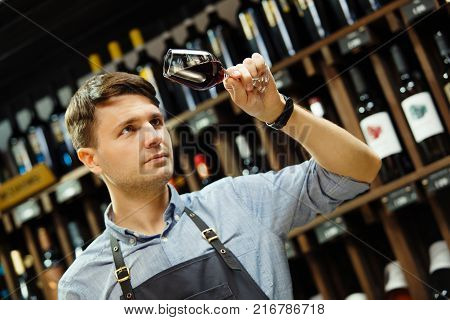 Bokal of red wine on background of male sommelier appreciating color, quality, flavor and sediments of drink. Professional degustation expert in winemaking.