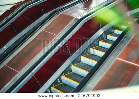 An empty moving escalator in subway. Escalator in metro. Moving up staircase. electric escalator. View through the greenery. Selective soft focus.