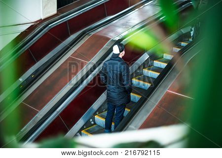 Back view man moving up on escalator in subway. Escalator in metro. Moving up staircase. electric escalator. View through the greenery. Selective soft focus