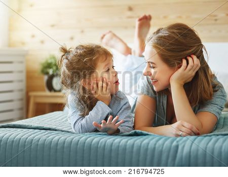 Happy family mother and child daughter play and laughing in bed