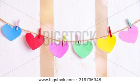 Multicolored hearts tied on a string - Cheerful image with colorful paper hearts with place for text on them tied to a linen string with wooden clips with a white wooden fence in the background.
