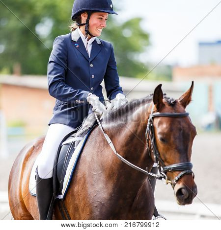Young happy woman on her bay horse after dressage test on equestrian competitions