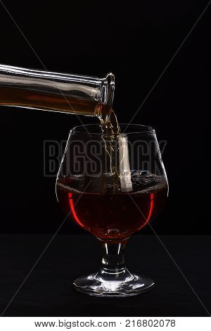 Brandy or cognac filling glass from bottle. Beverage for luxury occasions. Whiskey poured into low glass on black background. Drinkware and alcohol concept