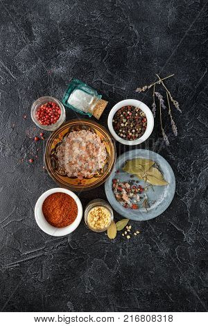 Pink, gold and white salt, black and red peppercorns, bay leaf, paprika on a black background Top view.