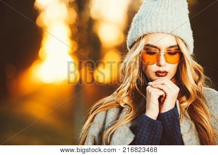 Autumn fashion. Fashionable young woman wearing warm sweater, a coat and a woolen hat posing in the park at a sunset.