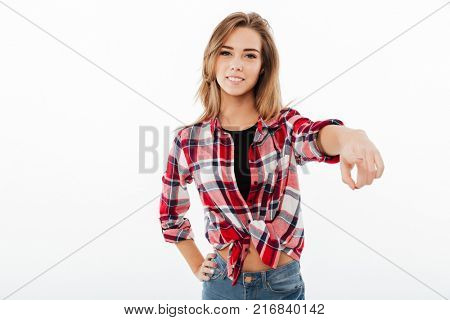 Portrait of a confident pretty girl in plaid shirt standing and pointing finger at camera isolated over white background