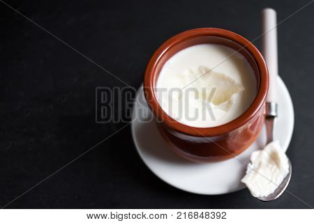 Sour cream or natural Cottage cheese curd in clay pot on dark background. Traditional Cuajada yogurt cream