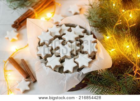 Cookies cinnamon star in a tin box on a background of cinnamon sticks, fir branches and cones. Selective focus.