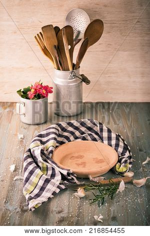 Empty Clay Plate On Wooden Board With Kitchen Utensils Around