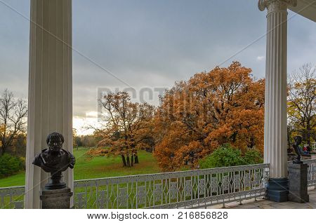 The view from the balcony with tall columns on a green meadow and autumn trees on a background cloudy sky