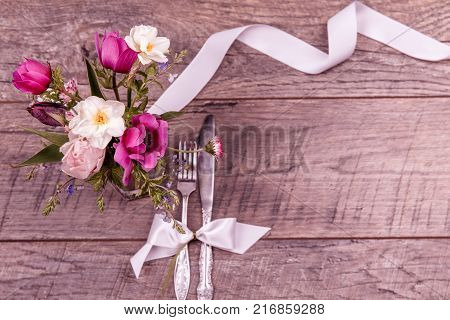 Place table setting with fork and knife, tied with a white satin ribbon, and flowers on a vintge table top view, flat lay, overhead, whith space for text