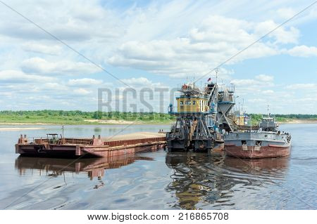 Volga, Russia. - June 2.2016. The floating dredger works deepens the bottom of the Volga River. Next to it is a barge loaded with sand and a river tugboat named ShS 11.