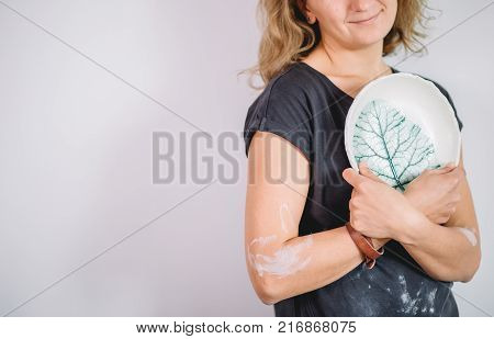 potter, tools, ceramics art concept - handsome young brunette female stand with finished utensils, smiling ceramist at workplace with baked cups and jugs at background