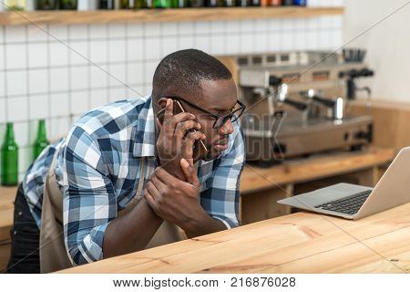 So attentive. Attentive responsible young worker feeling worried while looking at the screen of a modern laptop and talking on the phone with his employer