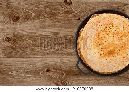 Crepes in a cast iron pan on dark wooden background top view