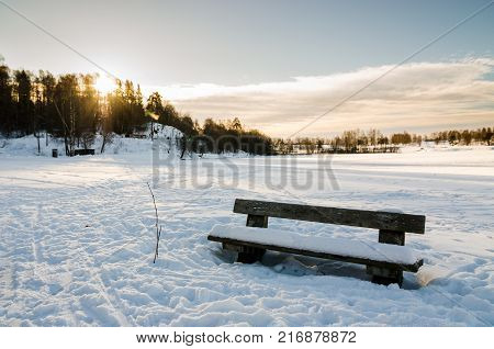 Wooden bench close to a frozen lake in Bogstadvannet Oslo. Winter low sun