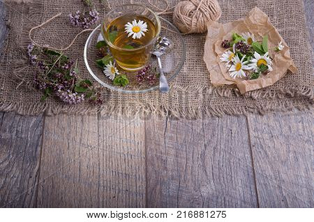 Cup of tea with chamomile ang origano flowers on rustic wooden background.