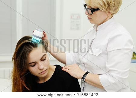 Doctor examines scalp a pretty young girl with special instrument UV lamp. Skin problems, dermatology, shingles, psoriasis, redness, prevention