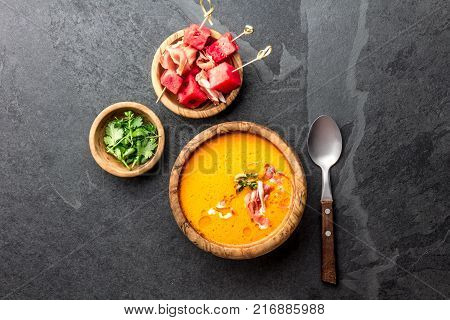 Salmorejo soup with watermelon. Traditional spanish cold tomato soup with watermelon and ham serrano in olive wooden bowl, slate background, top view.