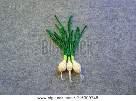 Three crocheted green onions on gray background. Texture of felt. Crocheted vegetables. Gray, white, green colors